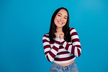 Smiling young woman holding hands, wearing a striped shirt, with blue background portraying happiness and positivity