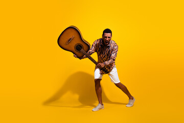 Young man enthusiastically playing guitar on vibrant yellow background symbolizing energy and...