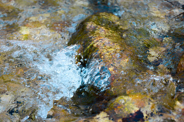 A close-up view of clear water rushing over a moss-covered rock in a natural stream.