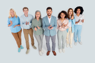 Diverse group of professionals standing together and clapping in a cooperative office atmosphere,...