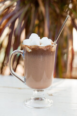 Warm hot chocolate with marshmallows in a glass mug outdoors