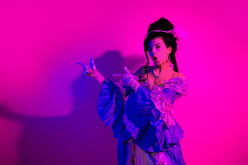 Naklejka premium Elegant lady in historical dress posing under vibrant neon pink lighting at a themed party