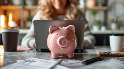 Obraz premium Woman using a laptop with a pink piggy bank on the desk. 