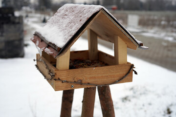A snowy birdhouse. It is made of wood and stands on three wooden legs.
