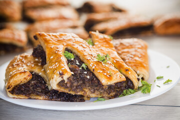 Golden puff pastries with mushroom filling and sesame seeds, on a light wooden table