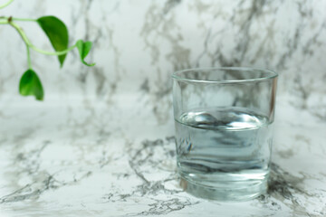 Tap water in glass pothos leaf on marble clean white background. Purity, rebirth, nature, healthy lifestyle, drinking more