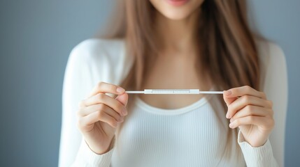 Woman holding pregnancy test while sitting on sofa indoors, close up, focus on hands
