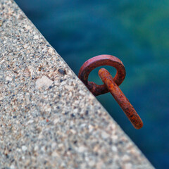 Rusty iron mooring ring for boat on concrete pier against sea water background