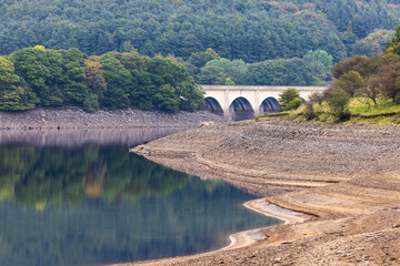 Dramatic low water levels at Ladybower Reservoir expose rocky shores, revealing the arched...