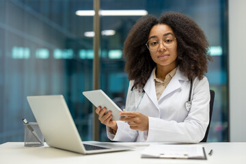 Portrait of serious confident female doctor at workplace inside modern clinic office. Female doctor...