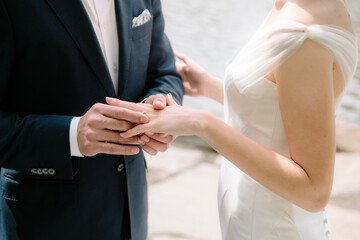 Couple exchanging wedding rings during a romantic outdoor ceremony near a serene water body