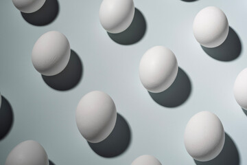 White eggs arranged on a light background with sharp shadows. Geometric composition with strong contrast, minimalistic aesthetic, and Easter theme.