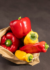 Close up of red bell pepper and pointed paprika in eco paper bag on grey table