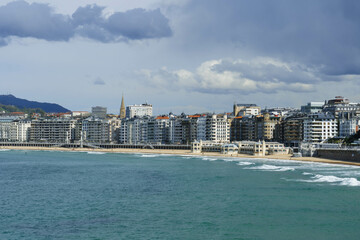 view of cantabria sea with waves on moody day in northern spain and city beach ahead