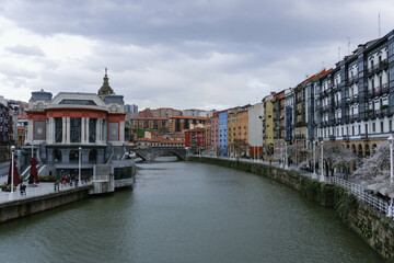 view of river in bilbao old town city center with many beautiful colorful houses on sides on cloudy day