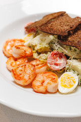 Appetizing Caesar salad with shrimp on a large white plate.