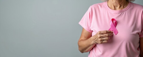 Elderly woman in pink T-shirt holds pink ribbon supporting people with breast cancer. Symbol of October awareness month, international women, mother day, oncology prevention, charity, healthcare.