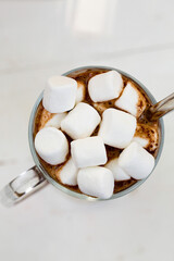 Hot chocolate with marshmallows in a glass mug on a white surface
