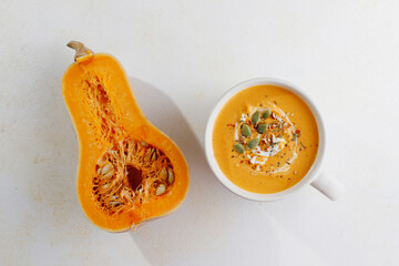 Roasted butternut squash soup with cream and pumpkin seeds on two white mugs.