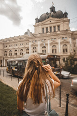 beauty girl with long brown hair of European appearance in summer in Ukraine in the city of Lviv during travel and vacation. Opera house and historical landmark