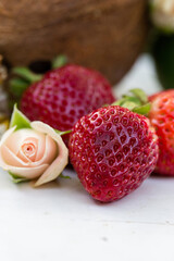 Fresh ripe strawberries with a delicate pink rose on a white surface