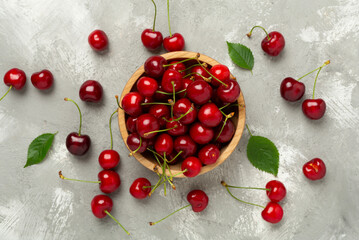 Fresh cherries in bowl on concrete background, top view