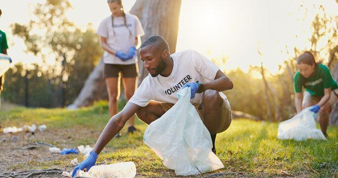 Volunteer, trash and man cleaning outdoor for community service, climate change or ngo at sunset. Charity worker, garbage bag or pick up plastic for recycling, pollution or waste management with team