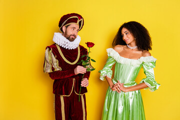 Couple in Elegant Historical Costumes Posing Against Yellow Backdrop
