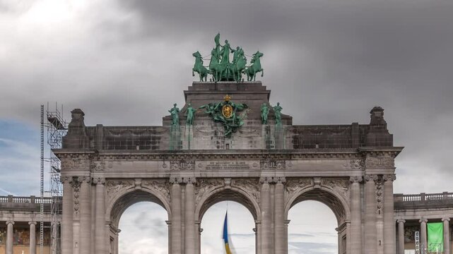 Timelapse of the Cinquantenaire Arcade in Jubelpark with flowerbed, Brussels, Belgium. The memorial triumphal arch stands tall under dramatic clouds, symbolizing Belgian history and independence.