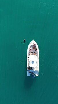 Aerial view of a boat in the blue ocean and people swim around in Hawaii top-down drone