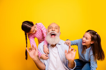 Happy grandfather enjoying playful moments with two energetic granddaughters on a bright yellow...