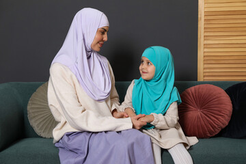 Muslim woman and her daughter sitting on sofa at home