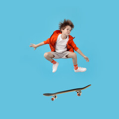 Obraz premium Cute little boy with skateboard in air on light blue background. Performing trick