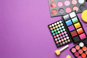 Face paints, tools and makeup products on purple background, flat lay. Space for text