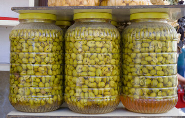 Big plastic jars preserving many green olives on a shelf, ready to be sold in a market