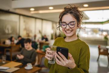 beautiful young woman hold glass of water and use mobile phone