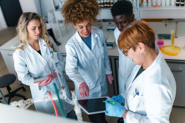 Group of diverse young science students and their professor working together, using a digital...