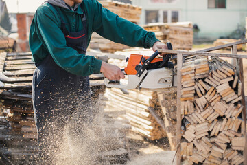 Employee working in a sawmill. 
A man cuts pallets of wood with a chainsaw.

