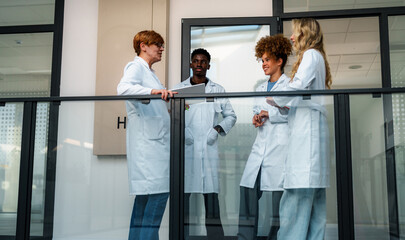 Professor and a diverse group of students in lab coats standing on a balcony, engaging in lively...