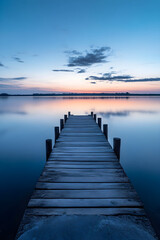 Naklejka premium Tranquil Pier Embracing Dawn Reflections with Weathered Wood and Gentle Waves in Serene Landscape