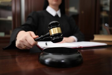 Judge striking gavel at wooden table in office, closeup