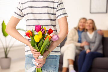 Boy hiding bouquet of tulips behind back for his parents at home, selective focus. Happy Mother's...