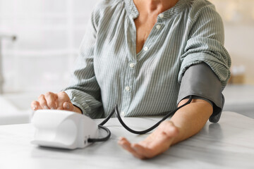 Senior woman measuring blood pressure at table in kitchen, closeup