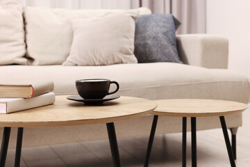 Nesting tables with cup of drink and books near sofa at home