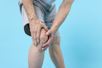 Senior man suffering from knee pain on light blue background, closeup