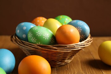 Beautiful decorated Easter eggs and wicker bowl on wooden table, closeup