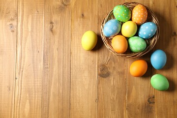 Beautiful decorated Easter eggs and wicker bowl on wooden table, flat lay. Space for text
