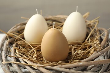 Egg-shaped candles in nest on light gray background, closeup. Easter decor