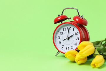 Spring time. Alarm clock and beautiful tulips on green background, space for text