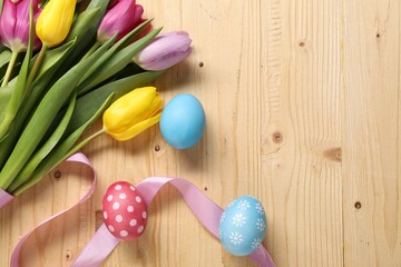 Easter eggs, beautiful tulips and ribbon on wooden background, flat lay. Space for text